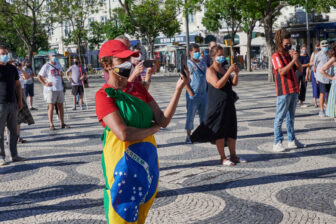 Woman wrapped in a Brazilian flag and red shirt and cap at a political rally in Portugal in 2020.