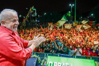 Lula is seen smiling on stage with supporters on the background