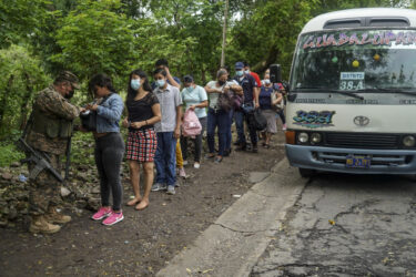 A line of civilians outside a bus in San Salvador wait to have their bags checked by soldiers.