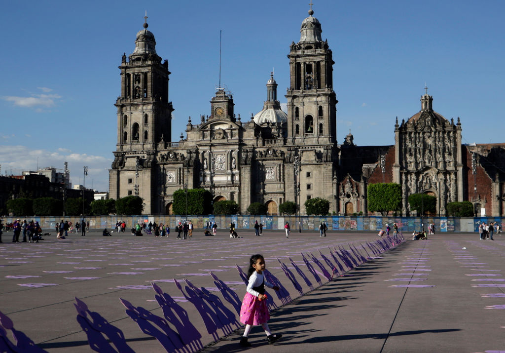 A girl walks by silhouettes of wooden women placed in front of the Metropolitan Cathedral in Mexico City to mark the International Day for the Elimination of Violence against Women on Nov. 25, 2023. Gender-based violence Is at the center of Mexico’s security crisis, and a recent mob attack underscores the need to recognize the gendered dimensions of violence in a critical election year.